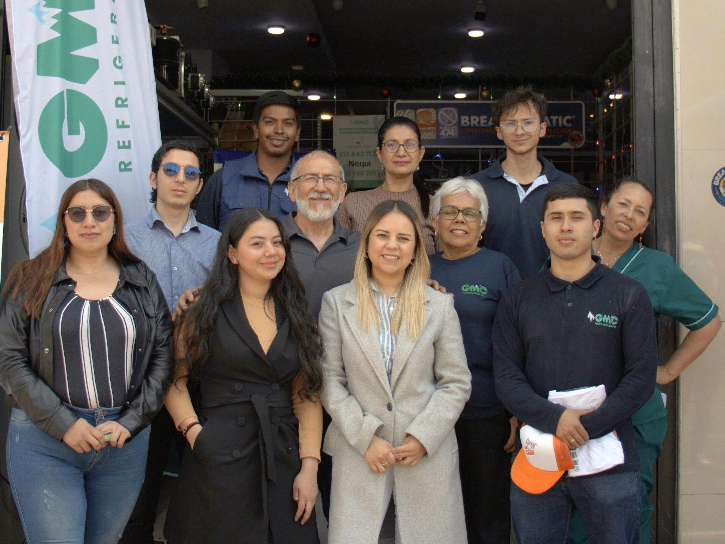 Once personas del equipo de GMC Refrigeración, administrativo y técnico, frente a su punto de venta en Bogotá, junto a una bandera con el logo de GMC